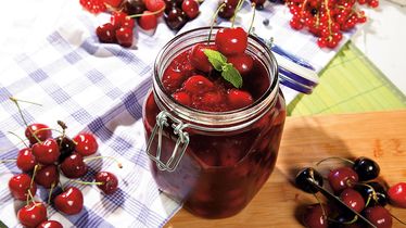 Ein Glas mit eingelegten Kirschen vom Foodservice, umgeben von frischen Kirschen und Johannisbeeren auf einem Holzbrett