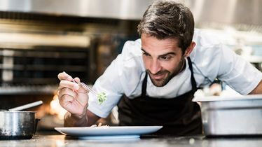 Ein Koch in einer Küche richtet sorgfältig ein Gericht auf einem Teller mit Zutaten von einem Foodservice an