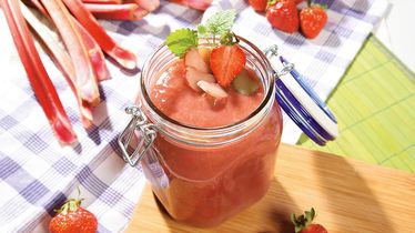 Ein Glas mit Rhabarber-Erdbeer-Konfitüre vom Foodservice, dekoriert mit frischen Erdbeeren und Rhabarberstangen