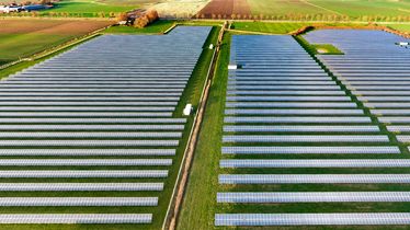 Solarpark aus der Vogelperspektive mit zahlreichen Solarmodulen in langen Reihen auf grünen Feldern