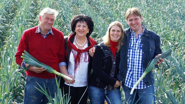 Zwei Männer und zwei Frauen, stehen in einem Lauchfeld und halten frische Lauchstangen aus Eigenproduktion.