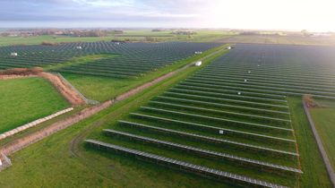 Luftaufnahme eines Solarparks mit Reihen von Solarmodulen auf grünen Feldern bei bewölktem Himmel