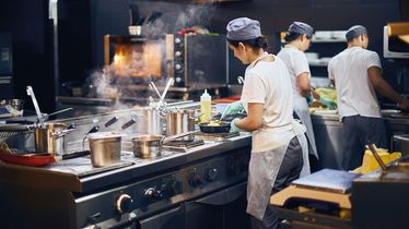 Köche arbeiten in einer Restaurantküche mit verschiedenen Kochutensilien und Lebensmitteln vom Foodservice